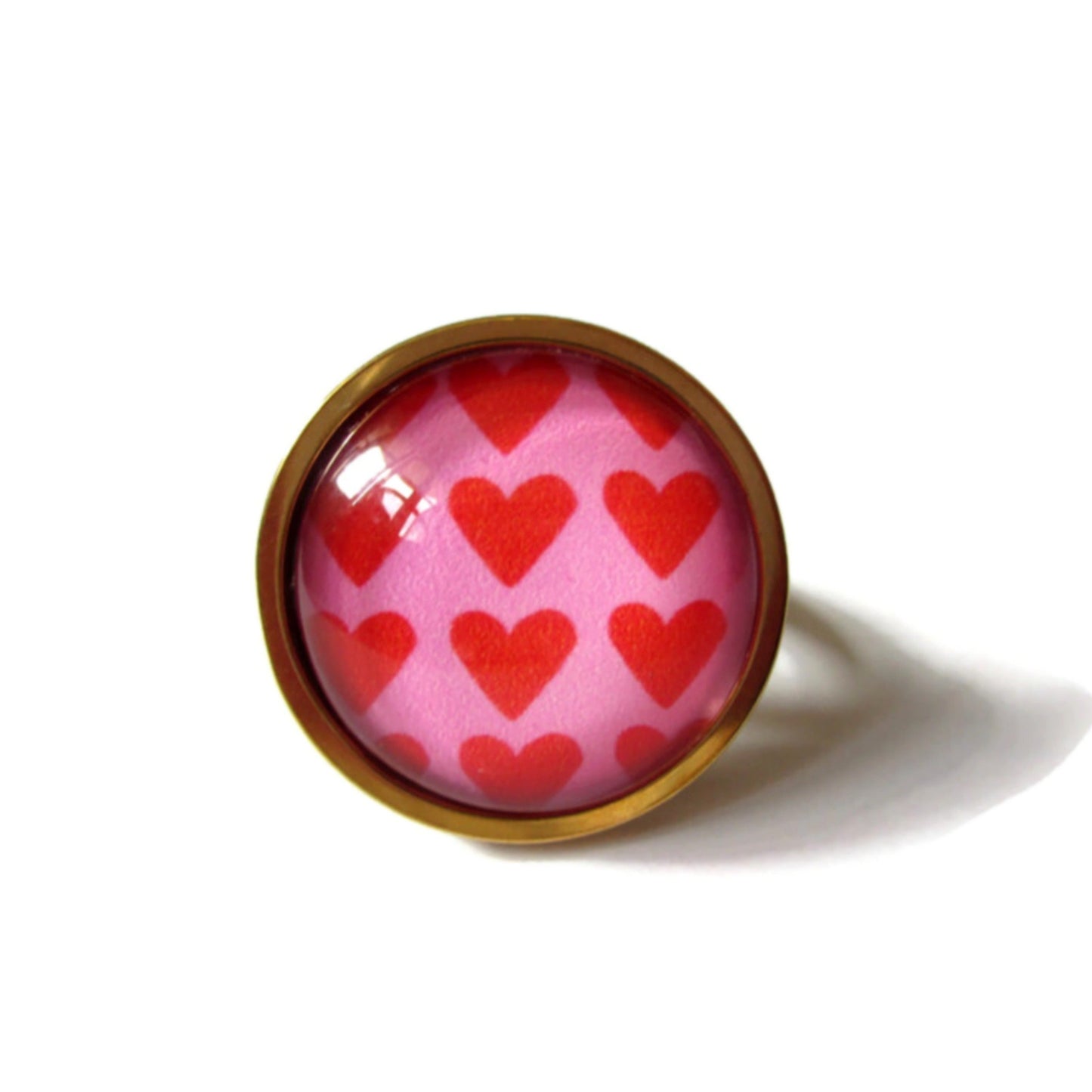 Bague dorée coeurs rouges sur fond rose